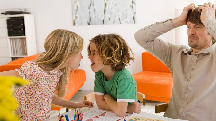 Zwei Kinder streiten sich am Tisch, ein Vater rauft sich die Haare