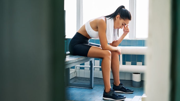 Niedergeschlagene Sportlerin sitzt in der Umkleidekabine