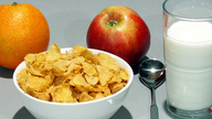 Eine Orange, ein Apfel, Milch und Cornflakes.