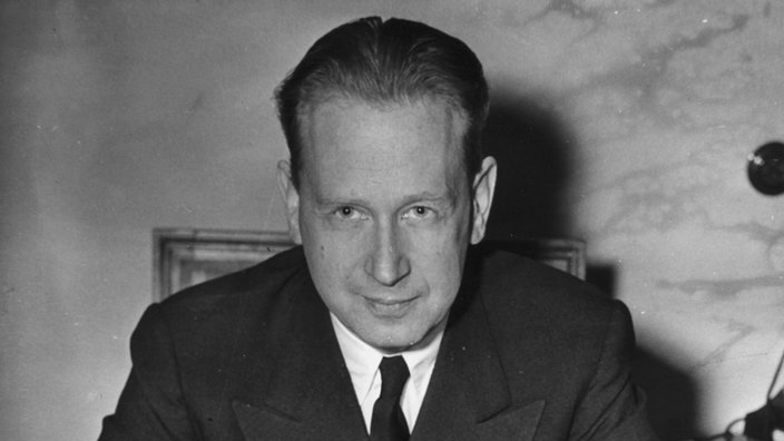 Dag Hammarskjöld sitzt an einem Schreibtisch und schaut in die Kamera.