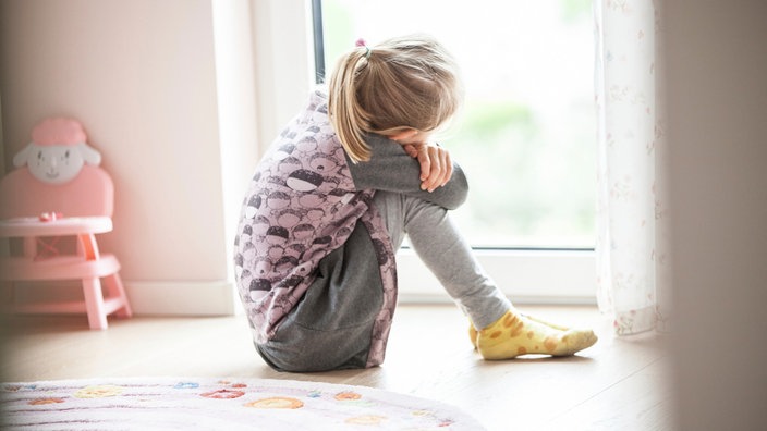 Ein Mädchen sitzt auf dem Fußboden eines Kinderzimmers.