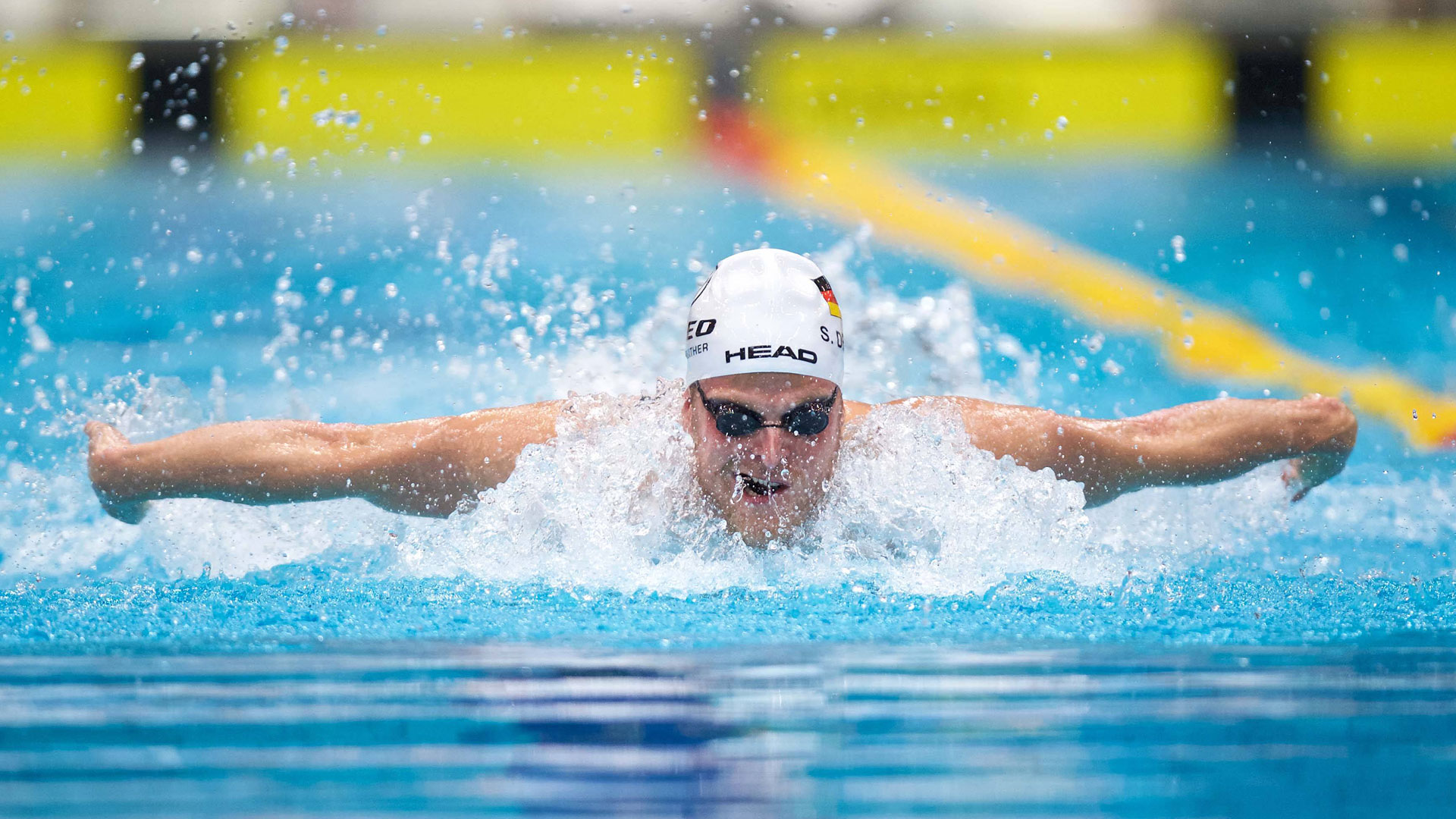 Schwimmer mit ausgebreiteten senkrecht vom Körper abstehenden Armen.