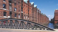 Blick über eine kleine Brücke auf die roten Backstein-Häuser der Speicherstadt.