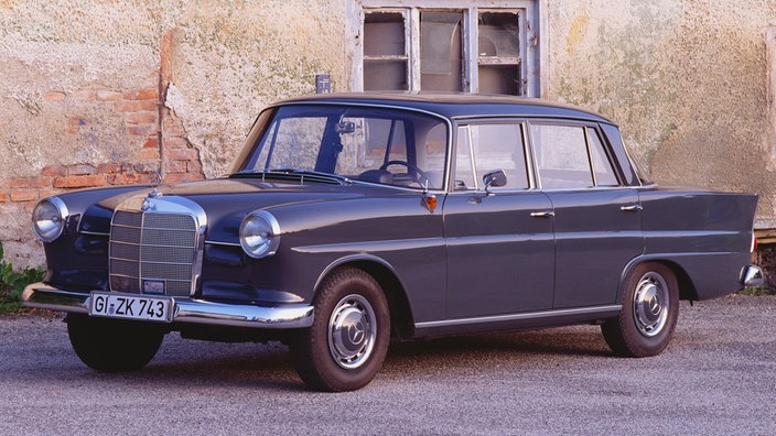 Ein dunkelblauer Mercedes-Benz "Heckflosse" aus den 1960ern vor einem alten Haus