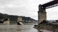 Pfeiler und Wrackteile der Brücke vom Ufer aus fotografiert. 