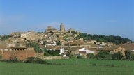 Blick auf ein kleines altes Dorf, das sich an einem Hang erstreckt, der aus der Ebene emporsteigt