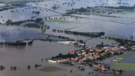 Luftbild: Die weit über die Ufer getretene Elbe ähnelt eher einem See als einem Fluss. Vereinzelt schauen Bäume aus dem Wasserteppich. Am Rand des Wassers ist ein Dorf zu sehen