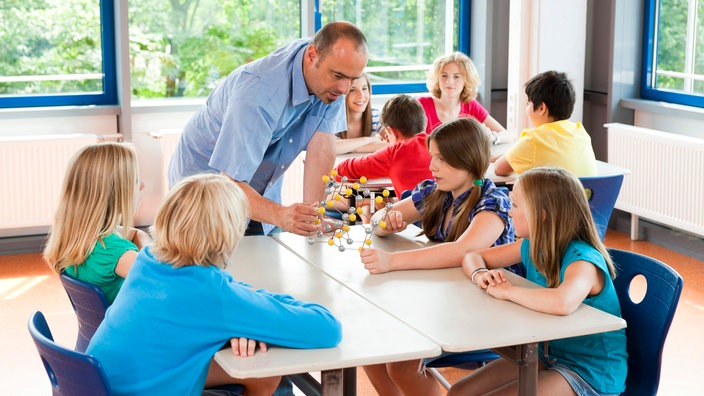 Ein älterer Lehrer erklärt einigen Schülern ein Molekülmodell.