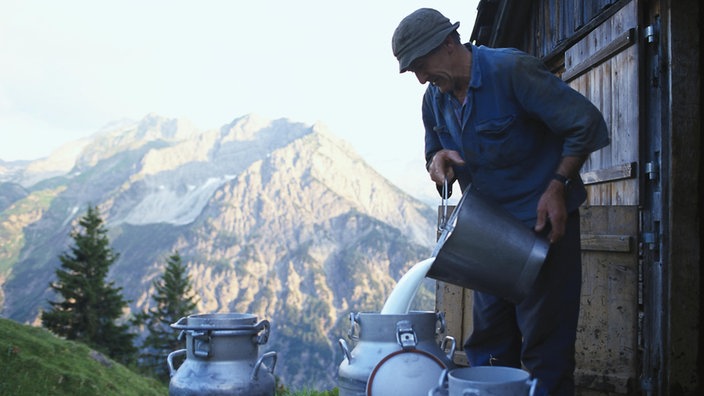 Ein Milchbauer füllt vor einer Hütte Milch in Milchkannen.