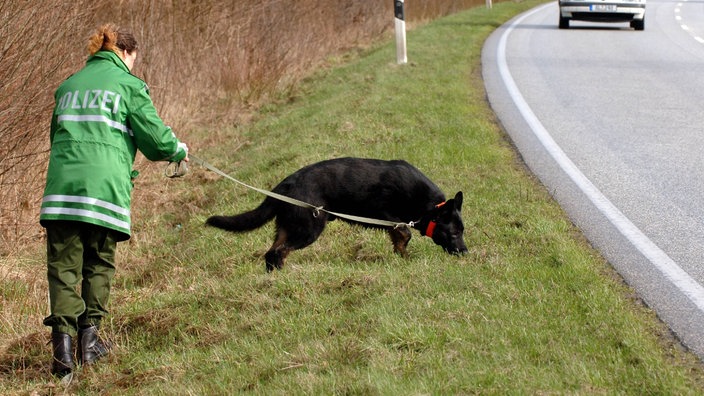 Eine Polizeibeamtin sucht mit ihrem Hund an einem Parkplatz nach Spuren.