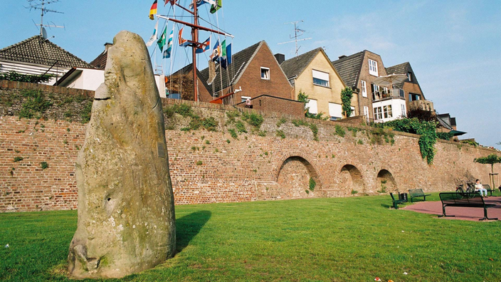 Ein Findling steht auf den Wiesen vor der Ufermauer am Rheinufer