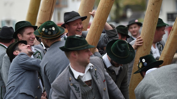 Traditionell gekleidete Männer stellen einen Maibaum auf.