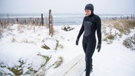 Frau in Taucheanzug steht am Strand.