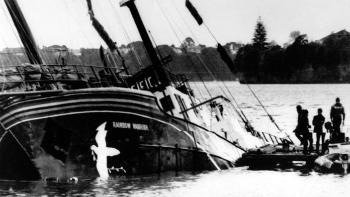 Schwarzweiß-Foto eines Schiffes, das auf der Seite im Wasser liegt und zu sinken droht