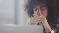 Gestresste Frau mit Händen vor ihrem Gesicht am Laptop.