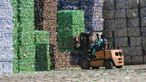 Mann mit Gabelstapler verlädt gepressten Plastikmüll