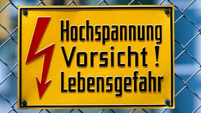 Ein Schild an einem Maschendrahtzaun weist auf die Gefahr durch Hochspannung hin