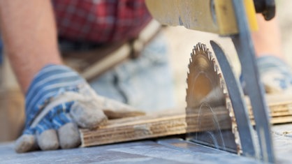 Arbeiter an einer Kreissäge bearbeitet ein Stück Holz. 